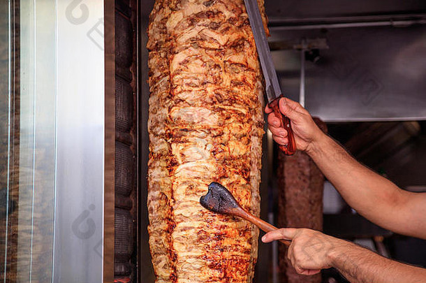 Gyros或doner，中东传统食品。男人的手拿着一把刀，从一个垂直的叉子上切薄片