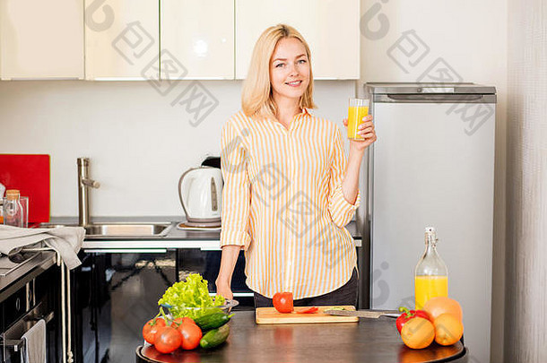 这张照片拍摄的是一位身穿条纹衬衫的年轻白人妇女，一边煮早餐一边喝鲜榨果汁。一个金发女孩正在厨房里享用美味的饮料