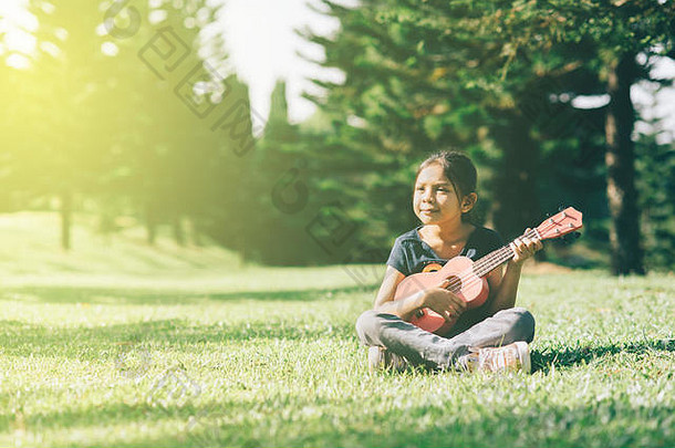 在阳光明媚的早晨，年轻快乐的亚洲女孩在公园里弹奏Ukelle<strong>吉他</strong>，同时寻找空间。爱好与宁静观
