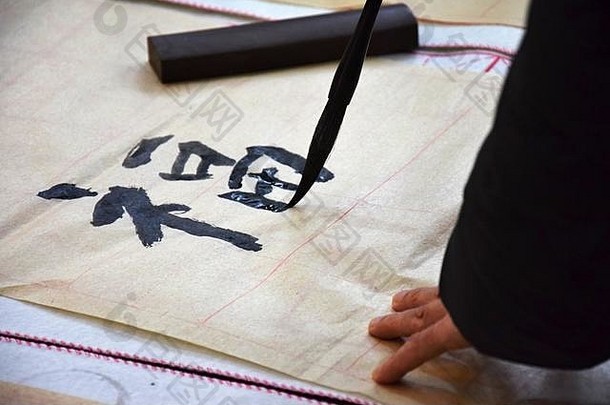 一只手拿着画笔，写着一个汉字福，幸福。在薄薄的纸上练习书法。