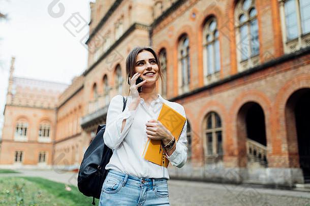 积极的浅黑肤色的女人女人休闲穿移动谈话校园书阳光明媚的一天微笑漂亮的赶时髦的人女孩会说话的电话每天