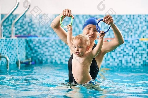 游泳教训婴儿妈妈。培训婴儿男孩游泳池色彩斑斓的环孩子持有环浮动水概念早期发展