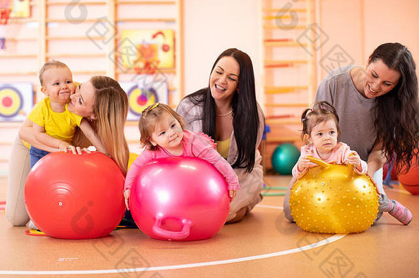 快乐的母亲和婴儿在健身房的健身球上。儿童健身球体操。