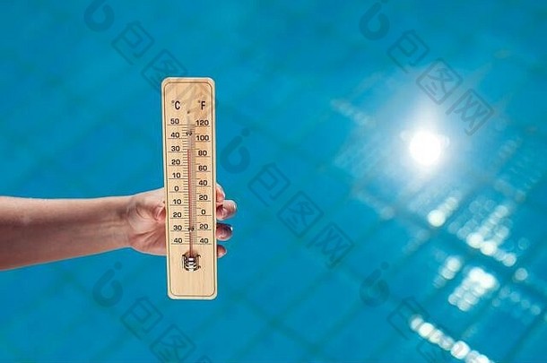 在蓝色泳池背景上拿着温度计的女人。炎热天气与夏季概念