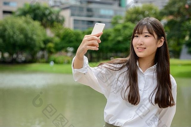 快乐年轻美丽的亚洲少女在公园自拍