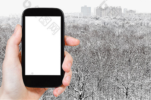 旅游理念-手持智能手机，屏幕镂空，背景为雪域森林和城市