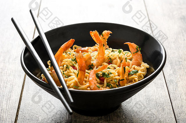 木桌上黑碗里的面条和蔬菜虾