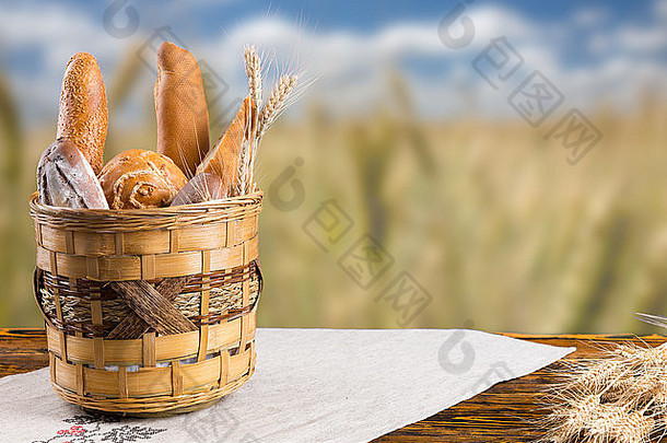 一篮各色新鲜的硬皮面包卷和面包放在一张古老的乡村木桌上，俯瞰着麦田