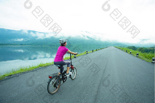 年轻的亚洲运动女孩早上在湖边骑自行车
