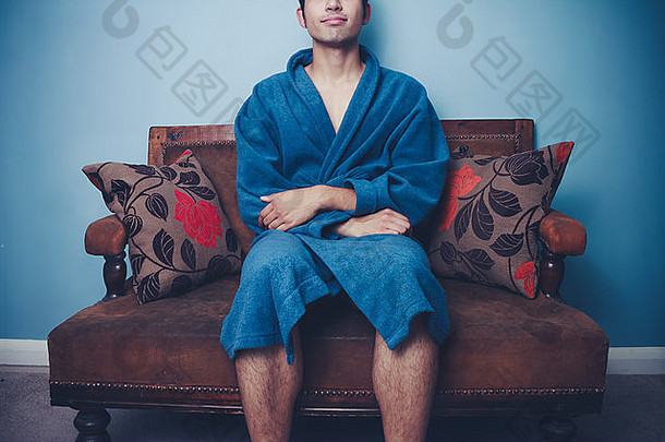 年轻的男人。浴袍坐着沙发放松