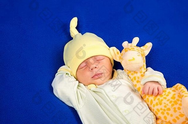 可爱的新生婴儿和玩具长颈鹿躺在蓝色毯子上。男孩还是女孩