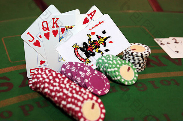 绿色桌上有筹码，扑克游戏中有皇家同花顺的<strong>手牌</strong>，包里有一个小丑