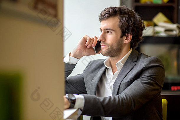 一个英俊的年轻商人坐在咖啡<strong>店</strong>的橱窗里，用着他的手机