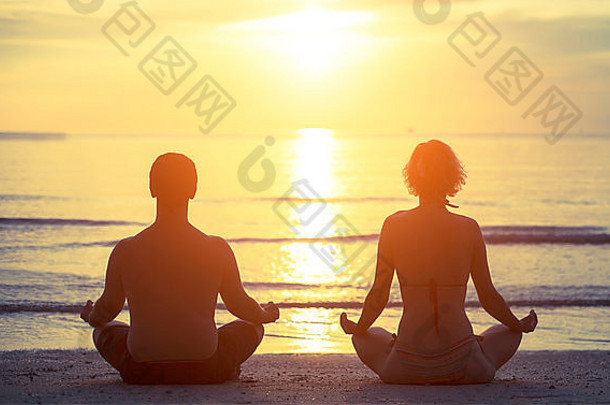 轮廓年轻的夫妇坐着瑜伽莲花位置银行海日落