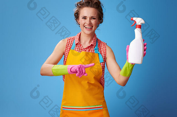 <strong>大扫除</strong>时间。穿着黄色围裙的快乐现代家庭主妇指着蓝色背景上的一瓶洗涤剂
