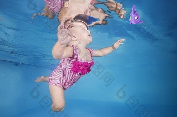 穿着粉红色泳衣的小女孩在游泳池里玩着玩具
