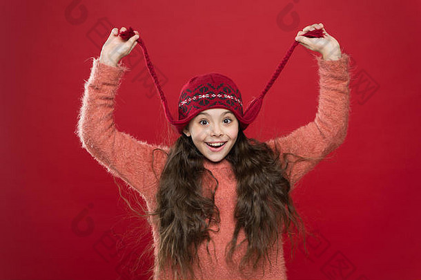 暖暖你的冬天。冬天的快乐孩子。小女孩戴着红色背景的针织帽子微笑着。小时尚模特喜欢冬天的风格。为孩子们准备的舒适<strong>冬季服装</strong>。