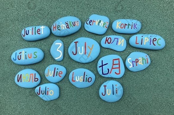 7月3日，绿色沙滩上彩色石头上的多种语言日历日期