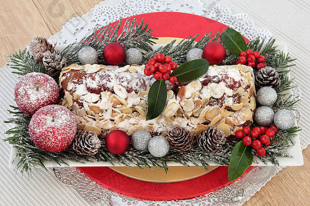 圣诞斯托伦蛋糕，冬青树，冷杉，装饰苹果和小玩意儿在银色的小垫子和橡木背景上的桌子。