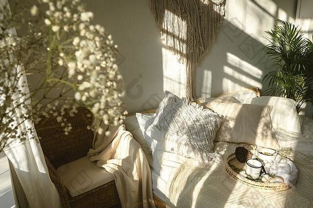 舒适的波西米亚风格阳光明媚的卧室，有灯光和阴影，白色石膏花特写。真实真实的室内设计