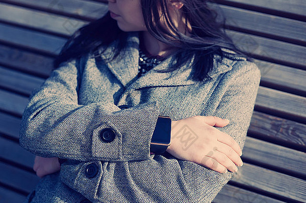 穿着灰色外套编织时尚智能手表的女士。此人<strong>始终</strong>连接到社交媒体和互联网。现代科技与复古时尚电影色调