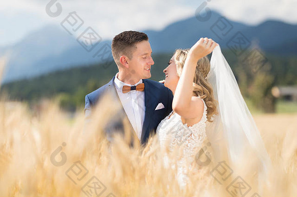 在斯洛文尼亚乡村的麦田里，新郎温柔地拥抱着新娘，微风吹拂着她的面纱。
