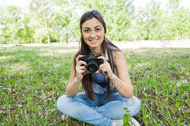 肖像微笑年轻的女人业余摄影师古董相机坐着草公园