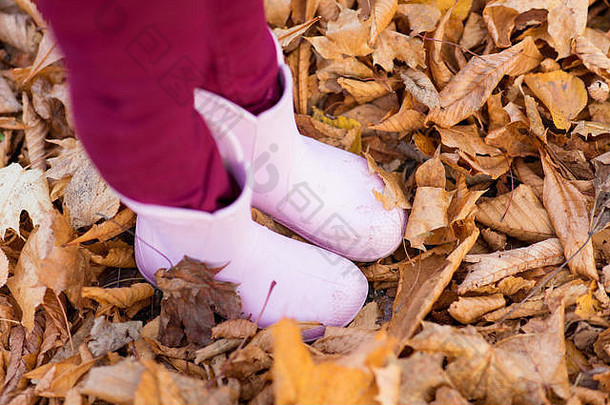 秋天树叶上穿着胶靴的小女孩的脚