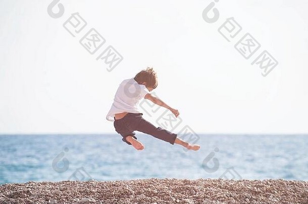 年轻的武术少儿师傅在日落的海滩上进行运动休闲训练活动，在空中踢腿