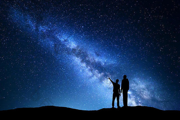 银河与男人的剪影。父亲和儿子在山上星空中指指点点。夜景。