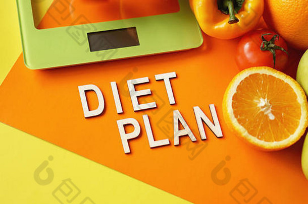 概念饮食。健康食品，厨房体重秤。橙色背景上蔬菜和水果刻字的饮食计划