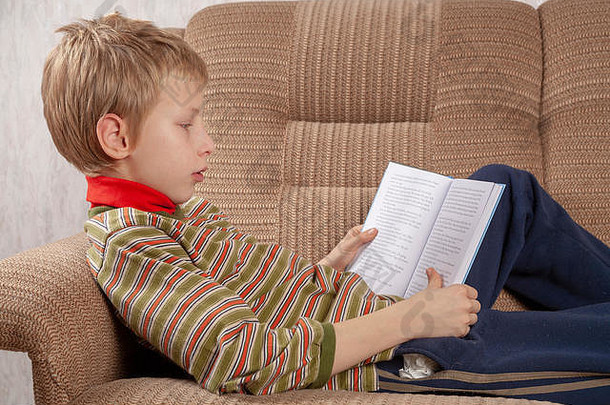 一个年轻的男孩躺在沙发上看书的肖像。