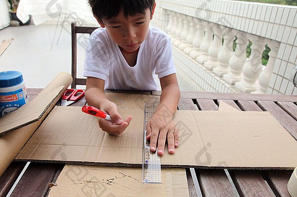 这是一张一个亚洲小男孩的照片，他正在用硬纸板做自己的工作，做火箭。他切割、粘贴和绘画。他是职业选手