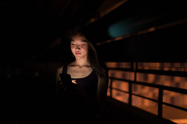 美丽的亚洲女人晚上在户外使用手机