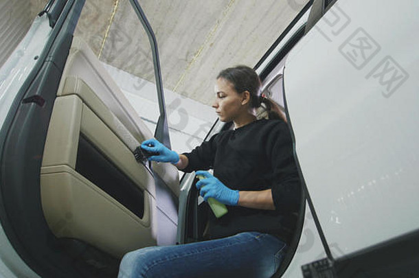 汽车清洁-一位漂亮的年轻女子正在用刷子清洗一辆豪华汽车的车门