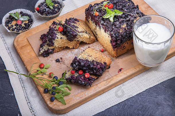 浆果蛋糕和松饼，蓝莓和草莓放在一个绿色的盘子里，一张木制的桌子上放着牛奶和新鲜的浆果
