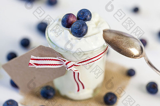 罐装凝块奶油或酸奶，新鲜蓝莓，用装饰丝带系好，空白礼品标签上留有文字空间，放在方形的麻布上，为健康的乡村美食服务