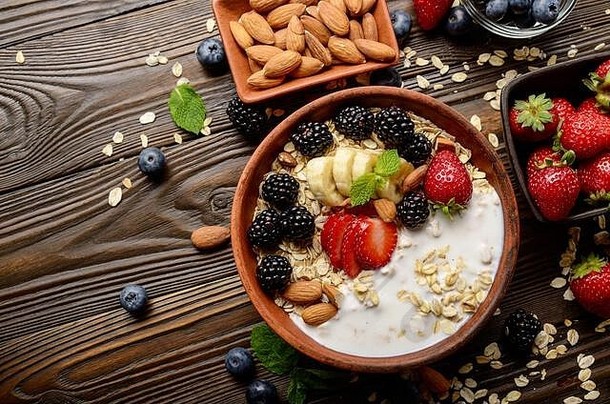 在木制厨房桌子上的粘土盘中，可以俯瞰水果健康的慕斯丽，香蕉、草莓、杏仁、黑莓和酸奶