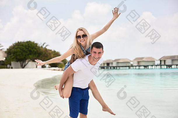 微笑的男人背着女人沿着海岸的肖像。那个在海上背着女朋友的家伙。一对年轻夫妇在一起玩得很开心