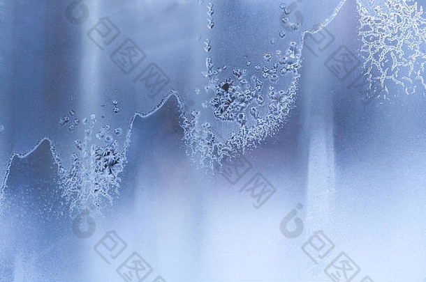 蓝色冰冻的冬季窗户上的波浪状奇异对角霜冻图案。