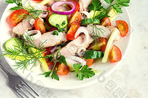 色彩斑斓的蔬菜沙拉，白色盘子上的肉（烤猪肉）和乡村风格的桌子水平收拢