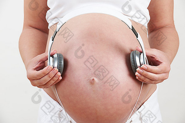 孕妇将耳机举到腹部的特写镜头