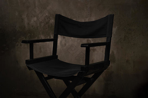 一把黑色的木椅子站在一个摄影棚里，背景是一堵被刮伤的旧水泥墙。
