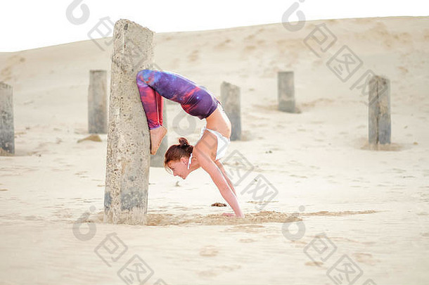 一位瑜伽修行者或瑜伽大师导师在日出时在海滩上锻炼，并在清晨展示她的力量、控制力和技巧。