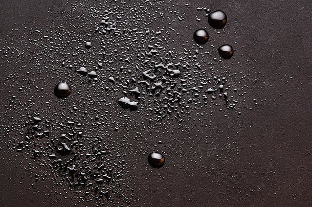 亮晶晶的水滴落在深褐色阴郁的表面上。抽象背景，俯视特写。