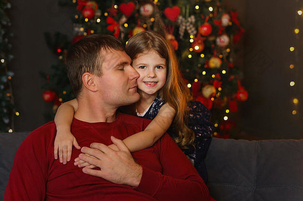 亲<strong>爱</strong>的爸爸和他的小女儿坐<strong>在</strong>家里的圣诞树旁。女儿轻轻地拥抱亲<strong>爱</strong>的爸爸。圣诞节家庭<strong>爱</strong>