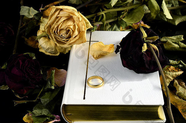 白色圣经，一枚结婚戒指和干玫瑰。感人的婚姻、死亡和至死不渝的概念形象使我们告别了结婚誓言。