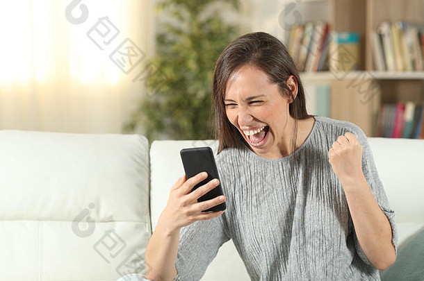 兴奋的女人坐在客厅的沙发上检查智能手机
