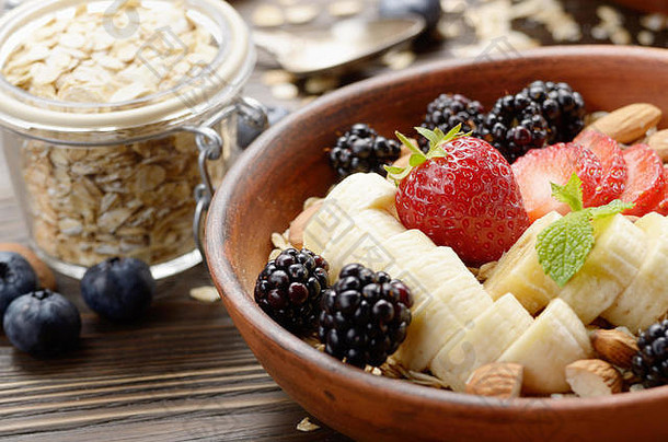 木制厨房餐桌上的粘土盘中有香蕉、草莓、杏仁和黑莓的水果健康<strong>慕斯</strong>里