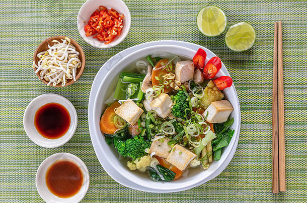 越南<strong>素面</strong>汤Pho装在白色圆碗中，配酱汁、酸橙、辣椒和豆芽。木筷在旁边。顶视图。